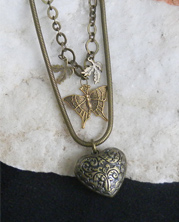 handmade designer necklace with deep textured heart of bronze colored metal hangs below a dainty bronze butterfly and leaves